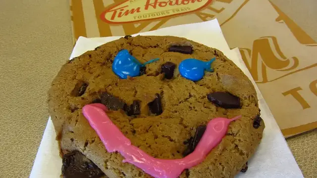 A Tim Hortons Smile Cookie with a pink icing smile and blue icing eyes
